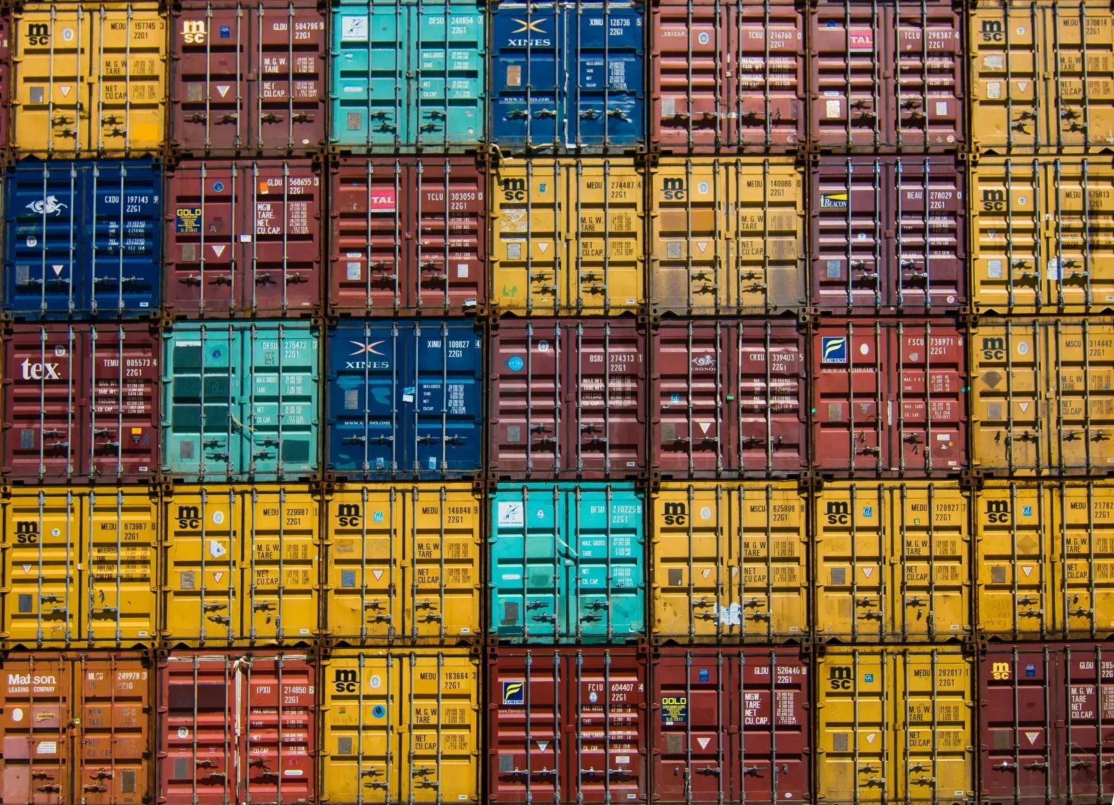 Bunte Seecontainer stehen dicht an dicht mit ihren Türen nach vorn übereinandergestapelt.