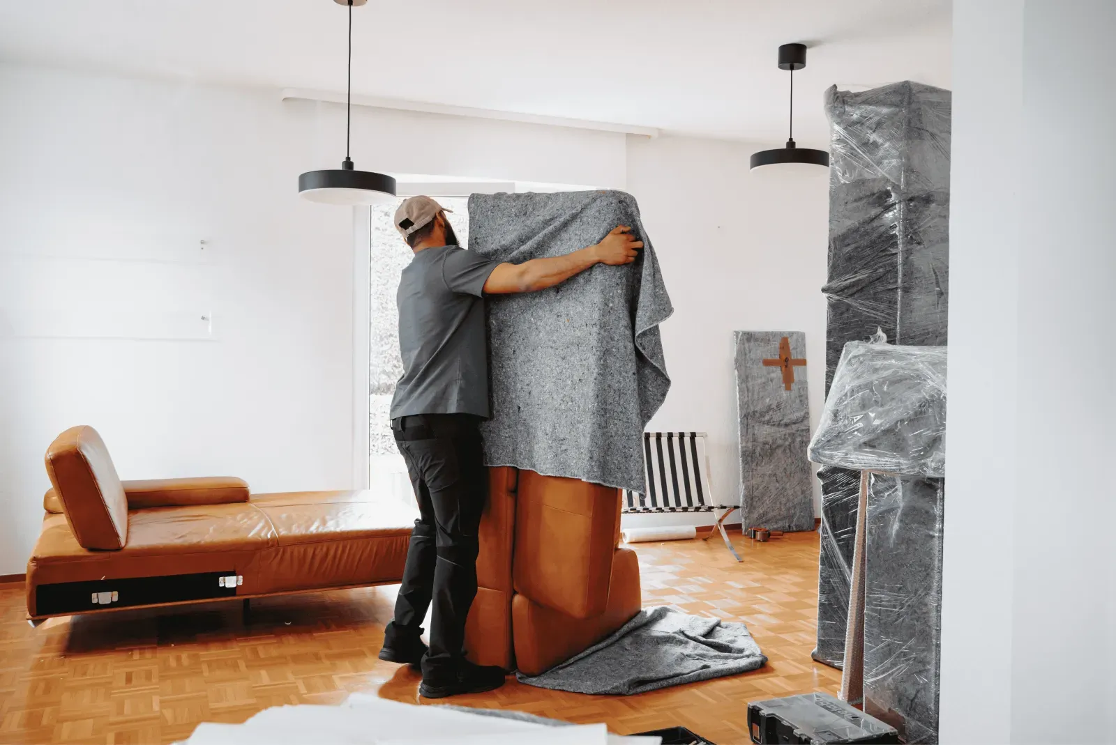 Ein Umzugshelfer umhüllt ein hohes Möbelstück mit einer Schutzdecke – Symbolbild