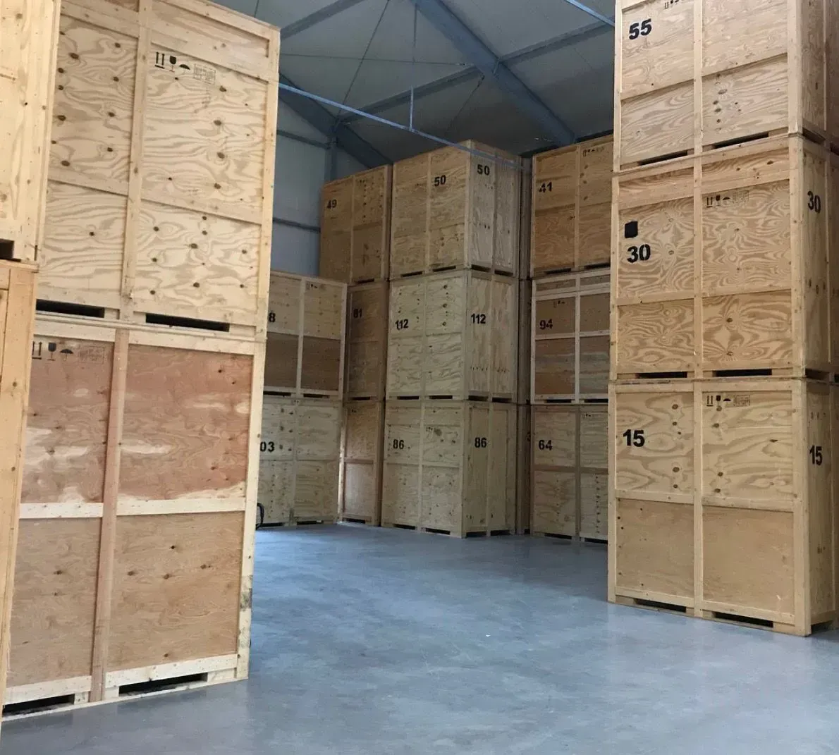 Große nummerierte Holzkisten stehen in mehreren Reihen und Ebenen in einer Lagerhalle.
