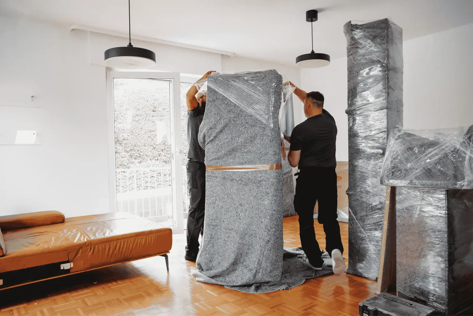 Ein Umzugshelfer sichert ein hohes Möbelstück mit einer Decke – Symbolbild